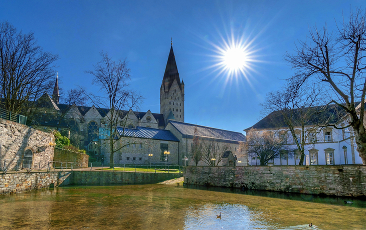 Kirche an einem sonnigen Tag mit klarem Himmel und Enten im Wasser.