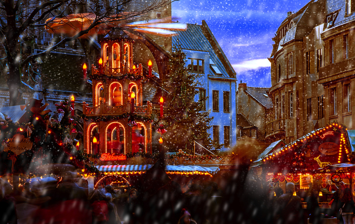 Voller Weihnachtsmarkt mit festlichen Lichtern und Menschen im Schnee.