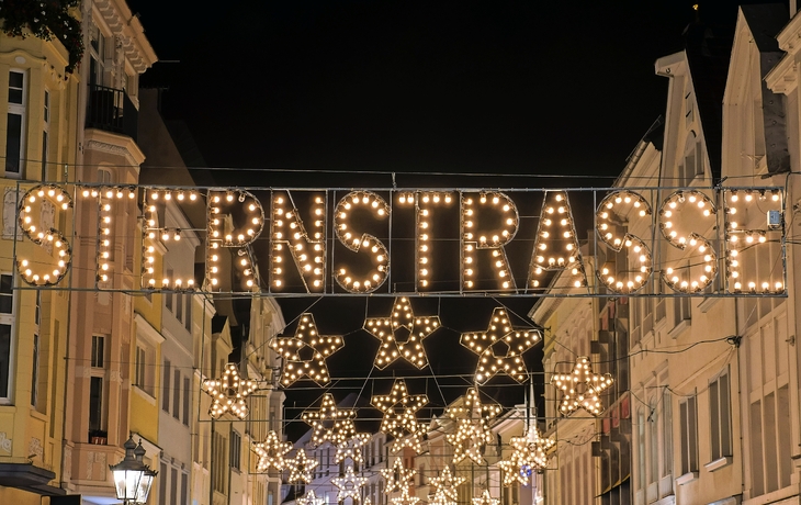 Beleuchtete Einkaufsstraße mit Stern-Dekorationen und Schriftzug "Sternstrasse" bei Nacht.