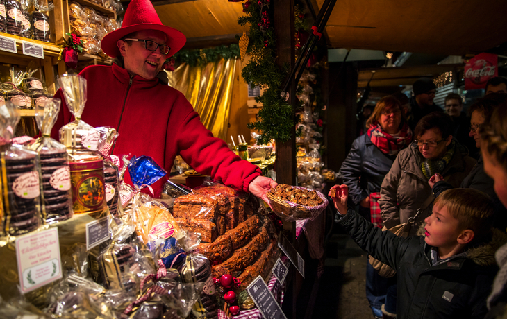 Verkäufer auf einem Weihnachtsmarkt reicht einem Kind Gebäck.