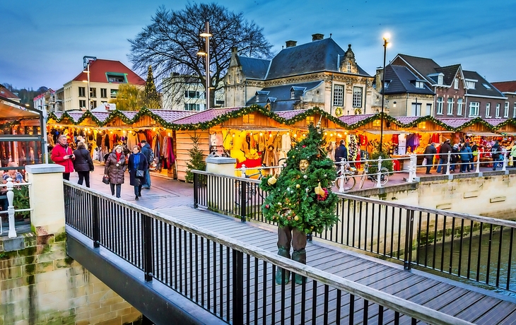 Weihnachtsmarkt mit Lichtern und geschmückten Ständen in einer Stadtumgebung.