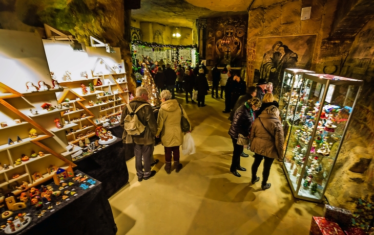 Besucher auf einem Weihnachtsmarkt in einer Höhle mit bunten Ständen und Dekorationen.
